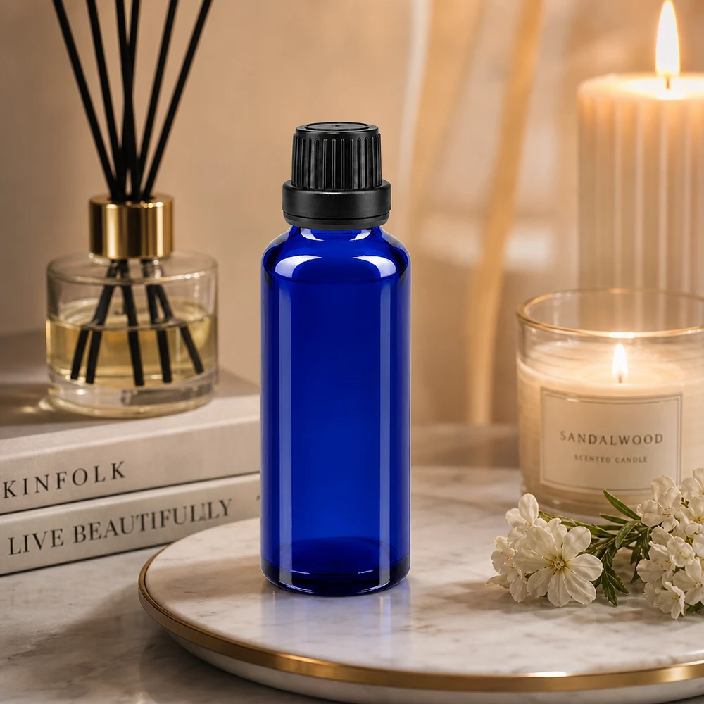Frasco de cristal azul de 30 ml con tapón OV negro sobre una bandeja de mármol, junto a una vela de sándalo y un difusor