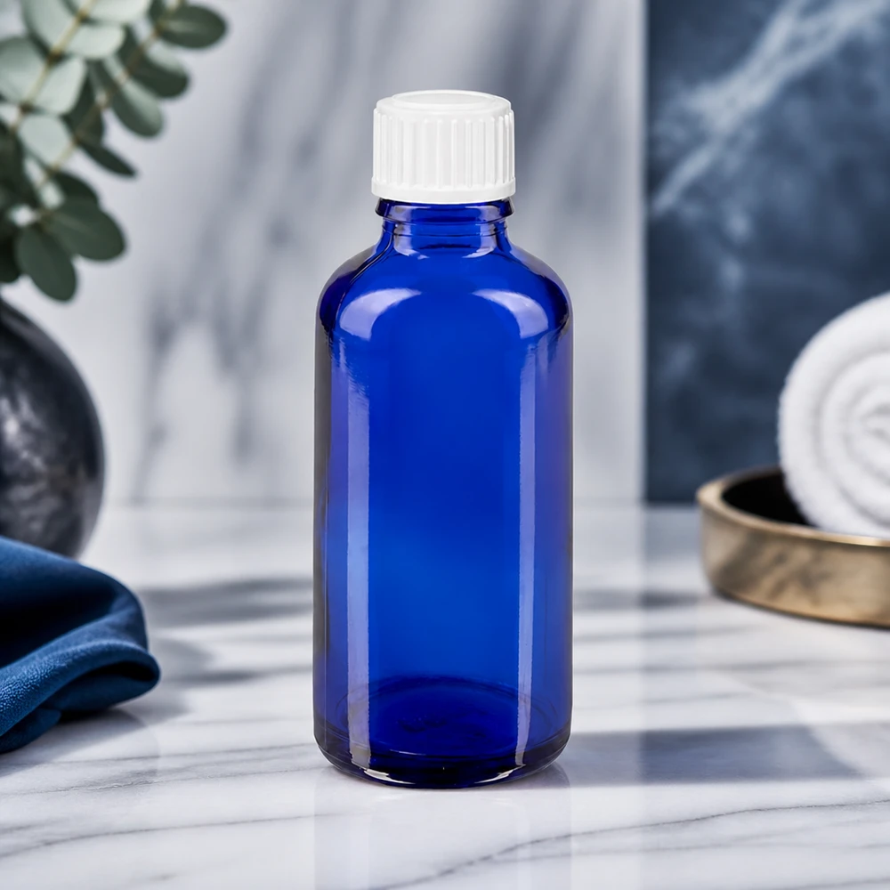 Frasco cuentagotas STD de 50 ml de color azul cobalto, fabricado por ApoGlas, con tapón blanco y superficie de mármol