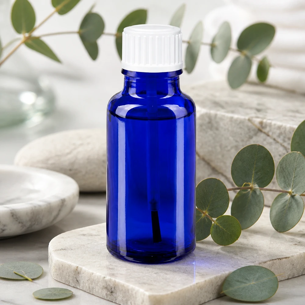 Botella de farmacia azul 20ml tapón rosca cepillo blanco Frasco de cristal azul cobalto de 20 ml con aplicador de pincel blanco sobre fondo de mármol y eucalipto