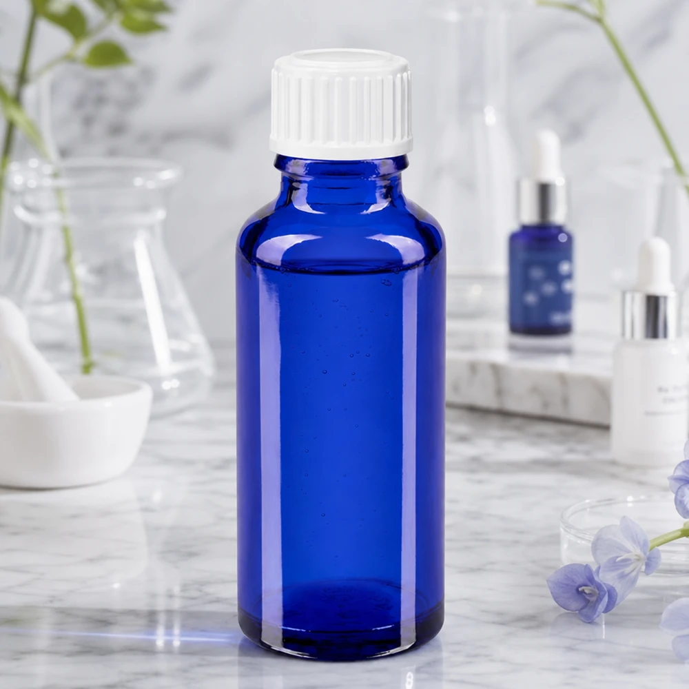 Frasco cilíndrico de vidrio farmacéutico de 30 ml en color azul cobalto con tapón de rosca blanco sobre fondo marmolado