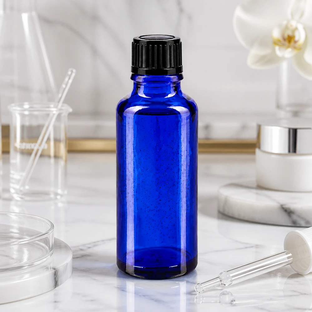 Frasco de cristal azul cobalto de 30 ml con tapón de rosca negro sobre fondo de mármol blanco