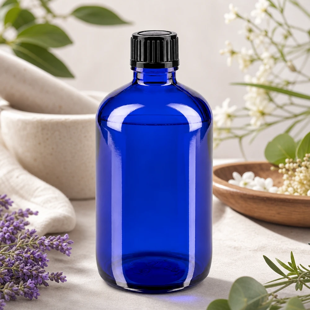 Botella de cristal azul de 100 ml con tapón de rosca, entre lavanda y flores blancas