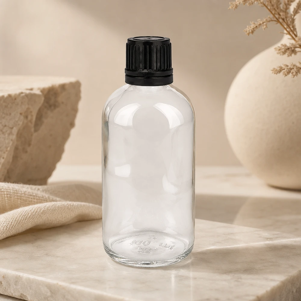 Frasco cilíndrico de cristal transparente de 100 ml con tapón negro estriado sobre fondo de mármol