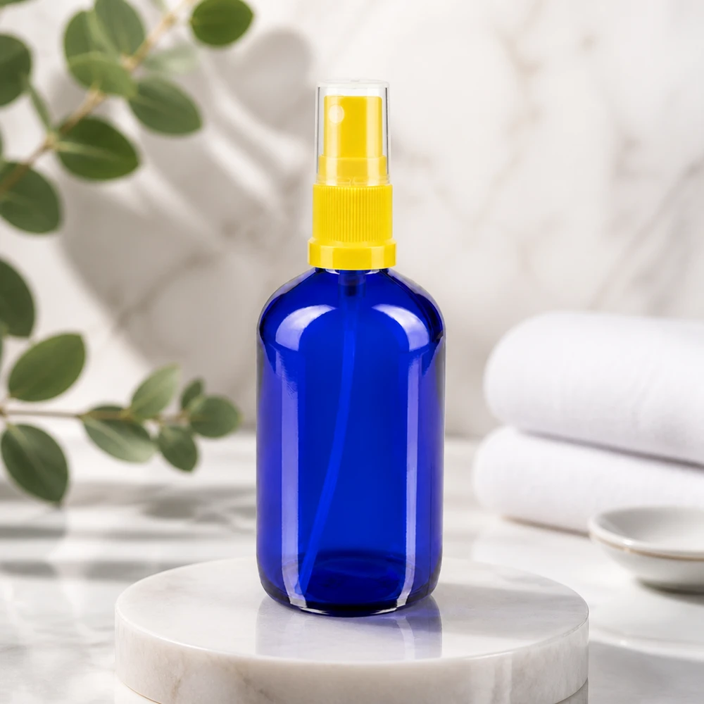 Frasco redondo azul de 100 ml, de cristal de farmacia, con pulverizador amarillo accionado con el dedo sobre una base de mármol