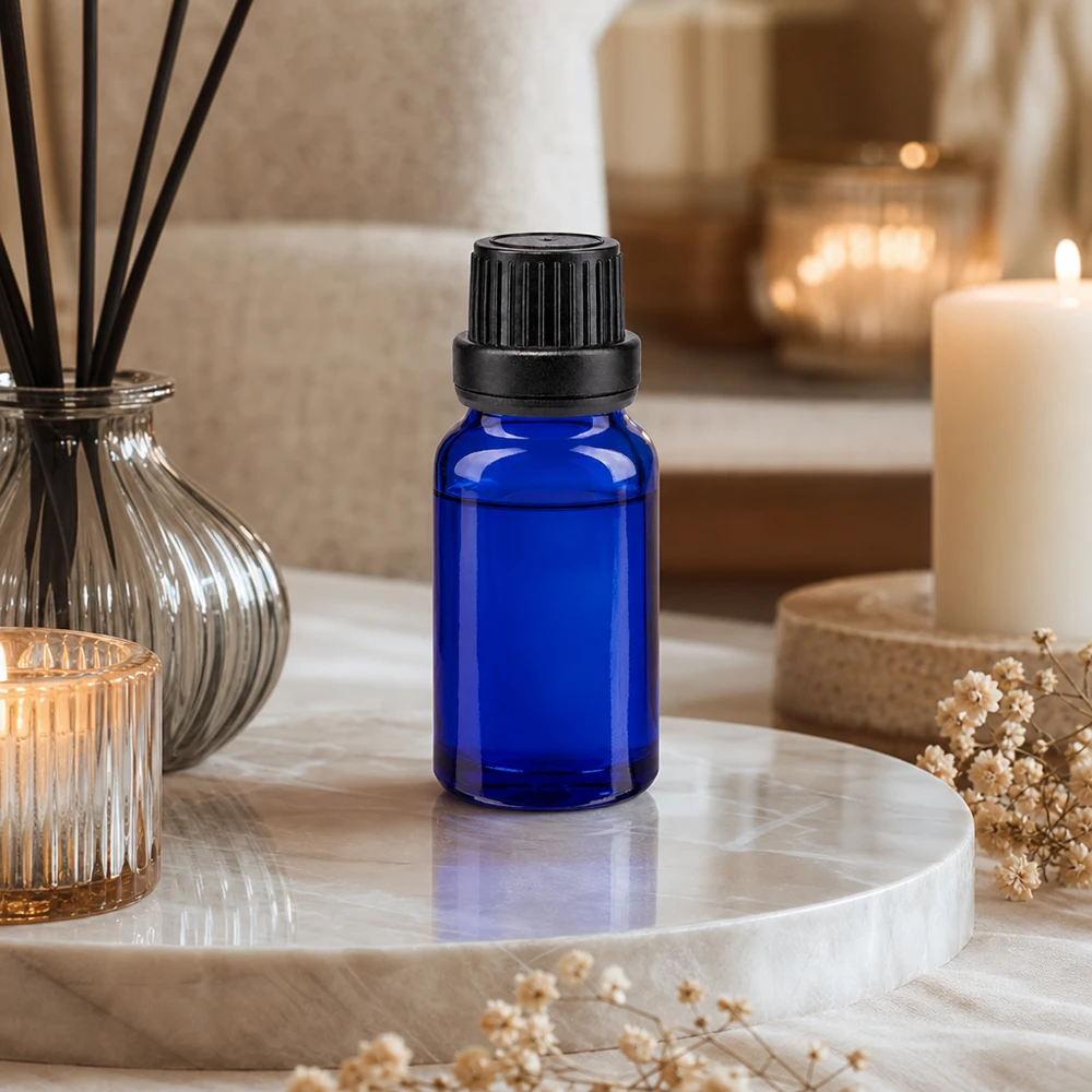 Pequeño frasco cuentagotas azul de cristal con protección UV, con un inserto de 2 mm, sobre una bandeja de mármol junto a unas velas