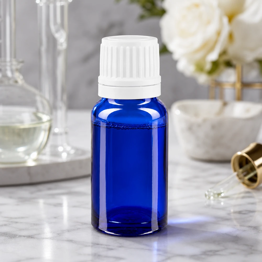 Frasco de farmacia de 10 ml de cristal azul con tapón cuentagotas blanco sobre una superficie de mármol, junto a unas rosas