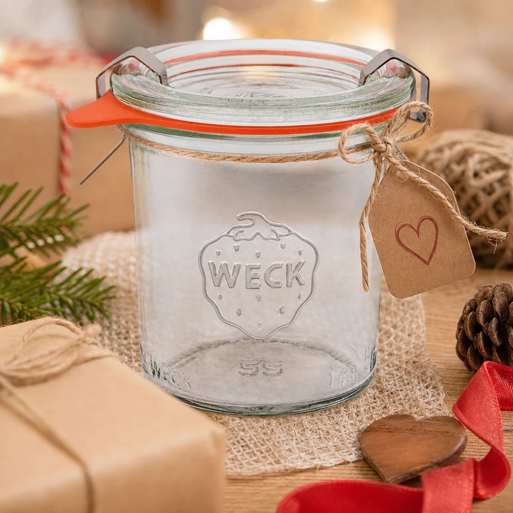 Vasos RR60 WECK de 140 ml como idea de regalo decorados con un colgante de corazón y cordón de yute sobre una mesa de madera con piñas de pino