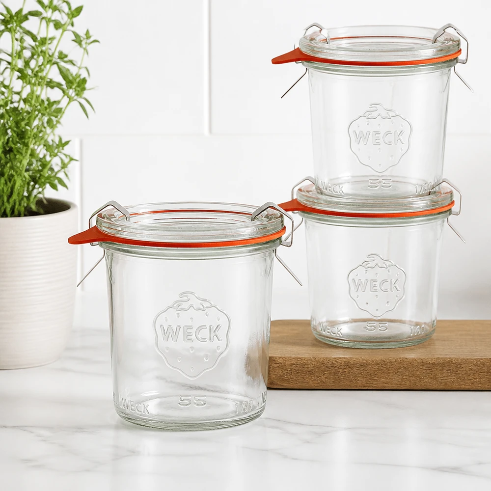 Tarro completo de 140ml WECK RR60 Tres vasos WECK RR60 de 140 ml apilados sobre una tabla de madera en una cocina moderna con una planta verde al fondo.