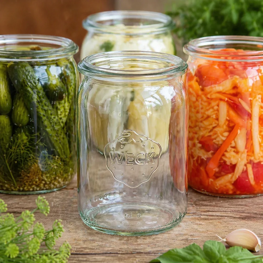 Tarro cilíndrico de 145ml WECK RR40 WECK tarro cilíndrico 145ml RR40 vacío entre tarros de conserva llenos con verduras encurtidas y fermentación sobre disco de madera