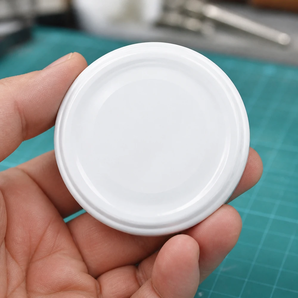 Tapa para tarros UNiTWIST TO43 blanca BioSeal sin BPA, vista desde arriba sobre una base de corte verde