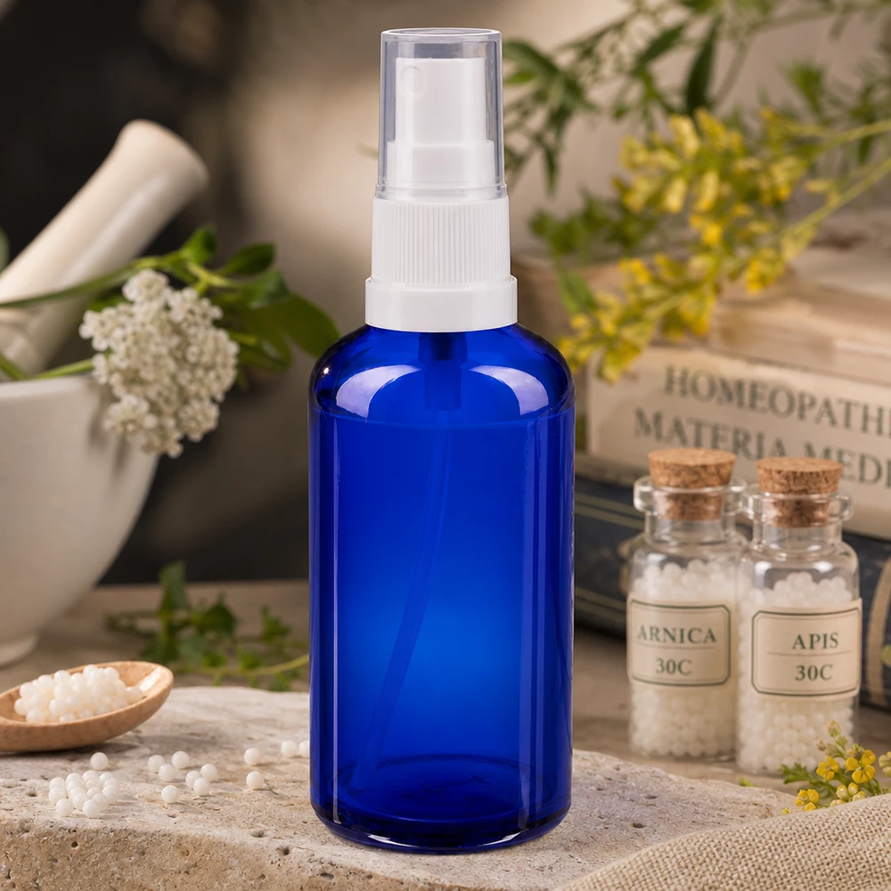 Frasco pulverizador de farmacia de cristal azul de 50 ml con dosificador blanco, junto a glóbulos homeopáticos